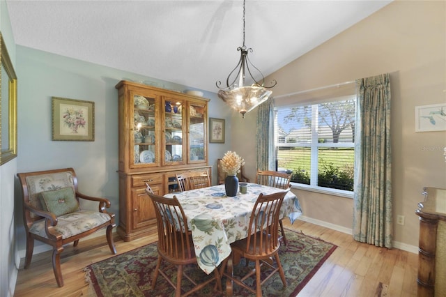 dining room with light wood-type flooring, an inviting chandelier, and lofted ceiling