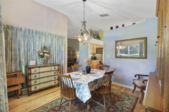 dining area featuring an inviting chandelier, vaulted ceiling, and light wood-type flooring