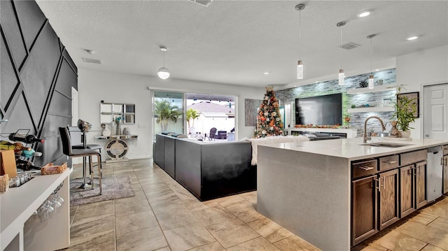 kitchen featuring a textured ceiling, dark brown cabinetry, sink, decorative light fixtures, and a center island with sink