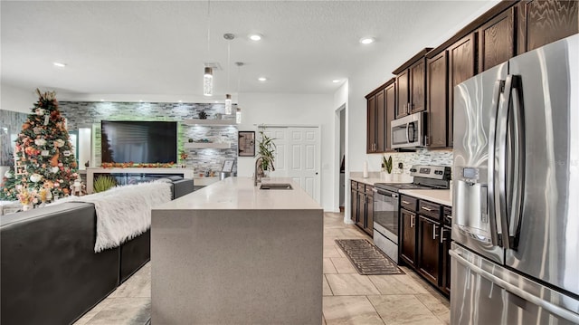 kitchen featuring dark brown cabinetry, sink, hanging light fixtures, an island with sink, and appliances with stainless steel finishes