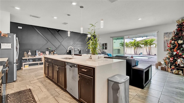 kitchen with dark brown cabinetry, stainless steel appliances, sink, a center island with sink, and hanging light fixtures