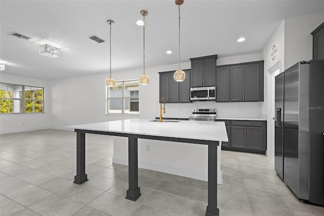 kitchen with backsplash, sink, hanging light fixtures, an island with sink, and stainless steel appliances