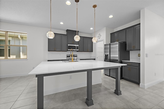 kitchen with hanging light fixtures, stainless steel appliances, backsplash, an island with sink, and gray cabinets