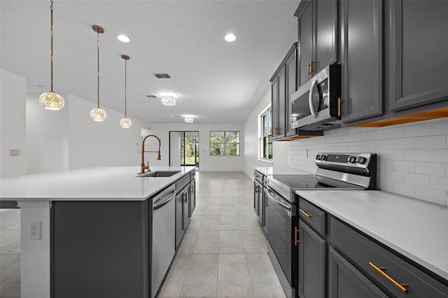 kitchen featuring sink, stainless steel appliances, an island with sink, decorative light fixtures, and gray cabinets