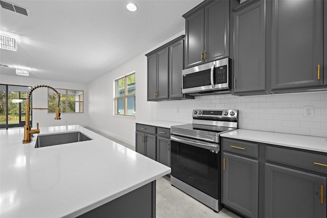 kitchen with appliances with stainless steel finishes, backsplash, gray cabinets, and sink