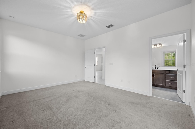 unfurnished bedroom featuring ensuite bathroom, sink, and light colored carpet