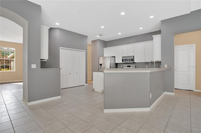 kitchen with white cabinets, light tile patterned floors, kitchen peninsula, and appliances with stainless steel finishes