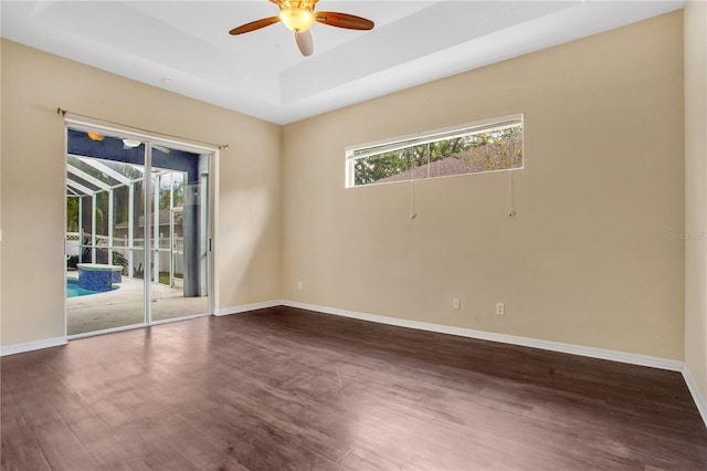 spare room with ceiling fan, a raised ceiling, and dark wood-type flooring