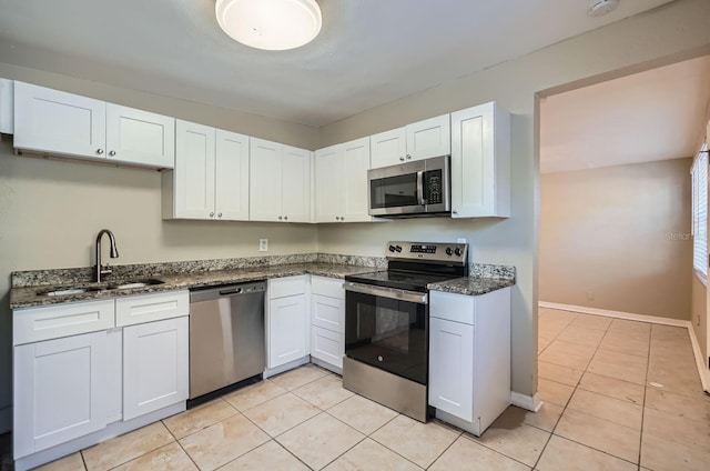 kitchen with appliances with stainless steel finishes, light tile patterned floors, dark stone counters, sink, and white cabinetry