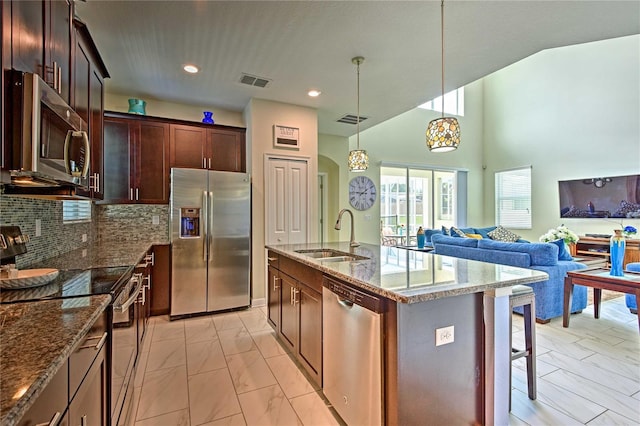 kitchen with appliances with stainless steel finishes, backsplash, a kitchen island with sink, sink, and decorative light fixtures