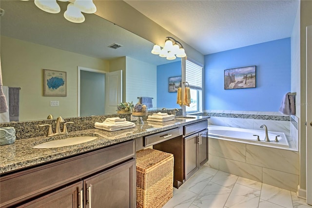 bathroom featuring a relaxing tiled tub, a textured ceiling, and vanity