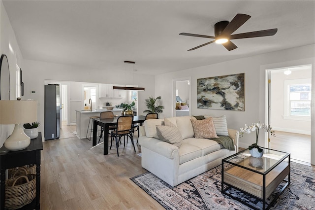 living room with light wood-type flooring, ceiling fan, and a healthy amount of sunlight