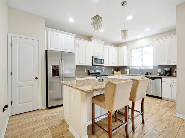 kitchen with white cabinets, a center island, stainless steel appliances, and hanging light fixtures