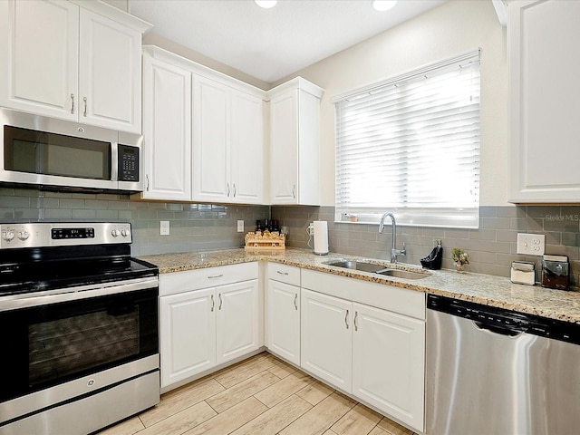 kitchen featuring tasteful backsplash, light stone counters, stainless steel appliances, sink, and white cabinets