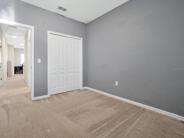 unfurnished bedroom featuring a textured ceiling, light colored carpet, and a closet