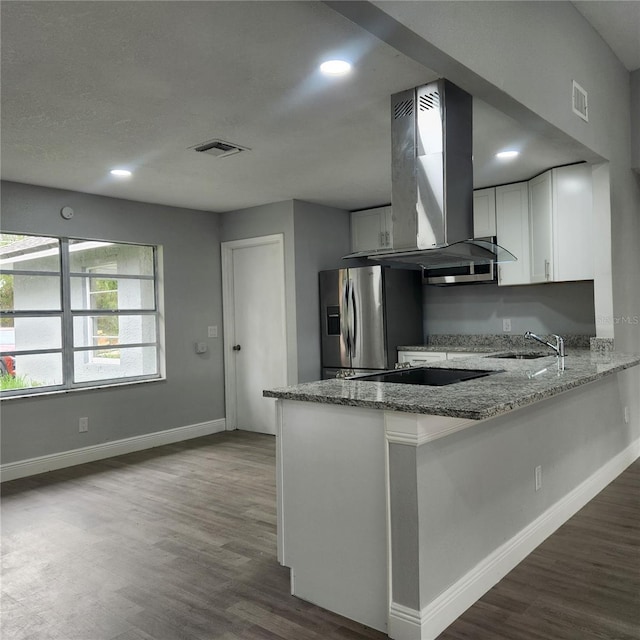 kitchen with a sink, light stone counters, stainless steel fridge, a peninsula, and island range hood