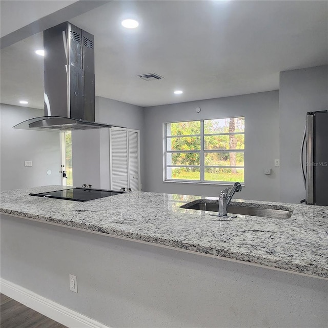 kitchen with visible vents, black electric stovetop, island exhaust hood, freestanding refrigerator, and a sink