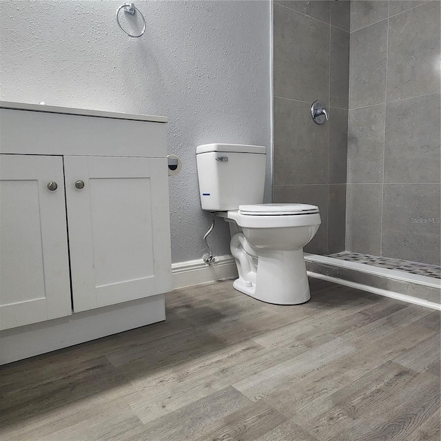 bathroom featuring a textured wall, toilet, wood finished floors, and a tile shower