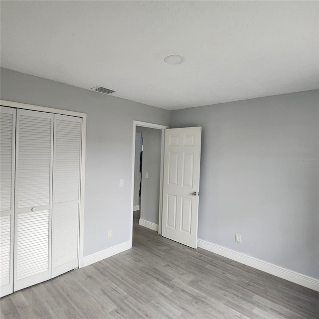 unfurnished bedroom with a closet, visible vents, baseboards, and wood finished floors