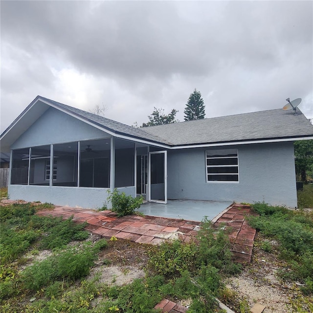 back of property featuring stucco siding, a shingled roof, a patio, and a sunroom