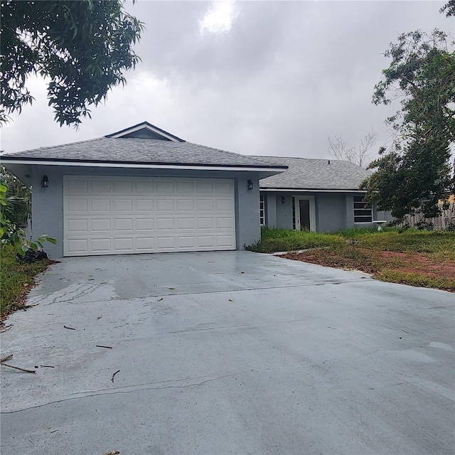 ranch-style home with stucco siding, roof with shingles, concrete driveway, and an attached garage