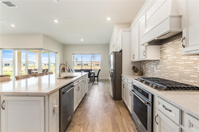 kitchen featuring sink, a breakfast bar, a kitchen island with sink, stainless steel appliances, and custom exhaust hood