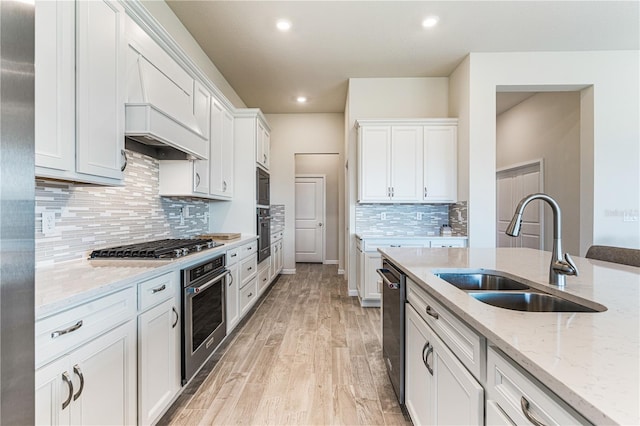 kitchen with sink, white cabinetry, light stone counters, appliances with stainless steel finishes, and light hardwood / wood-style floors