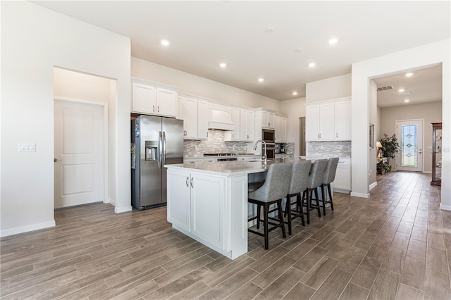 kitchen featuring appliances with stainless steel finishes, custom range hood, a center island with sink, and white cabinets