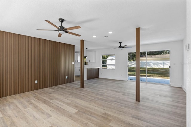 unfurnished living room featuring a textured ceiling, light wood-type flooring, ceiling fan, and wood walls