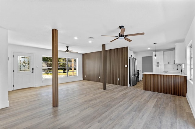 unfurnished living room featuring light hardwood / wood-style flooring, ceiling fan, and sink