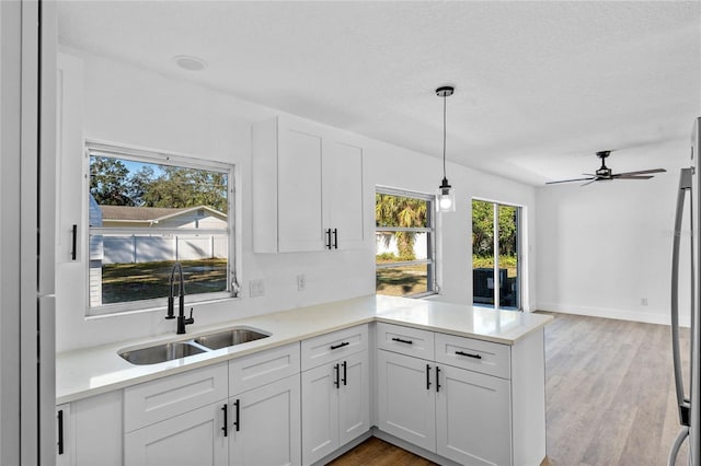 kitchen with kitchen peninsula, sink, hanging light fixtures, hardwood / wood-style flooring, and white cabinetry