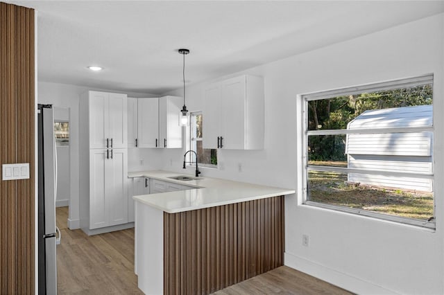 kitchen featuring pendant lighting, kitchen peninsula, white cabinetry, and sink