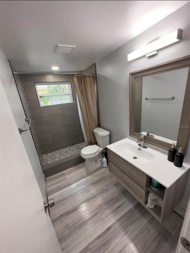 bathroom with wood-type flooring, vanity, toilet, and curtained shower