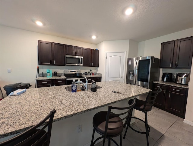 kitchen featuring a kitchen breakfast bar, light stone counters, dark brown cabinets, stainless steel appliances, and light tile patterned floors