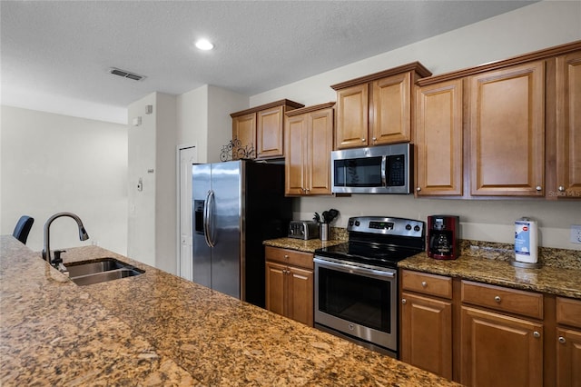 kitchen with appliances with stainless steel finishes, sink, a textured ceiling, and dark stone countertops