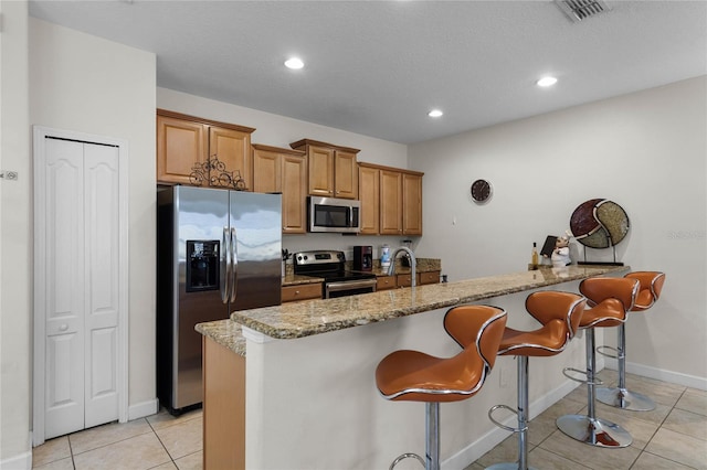 kitchen with sink, appliances with stainless steel finishes, light stone counters, a kitchen bar, and light tile patterned flooring