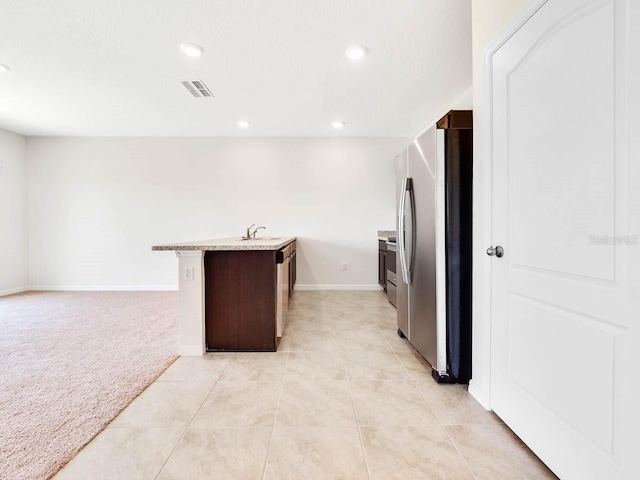 kitchen with a center island with sink, sink, stainless steel fridge, dark brown cabinets, and light colored carpet