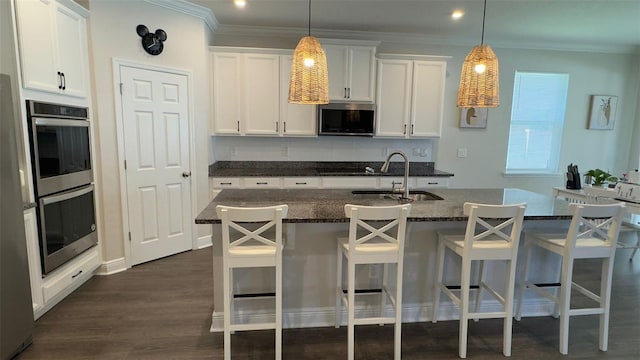 kitchen featuring dark stone counters, stainless steel appliances, sink, white cabinets, and an island with sink