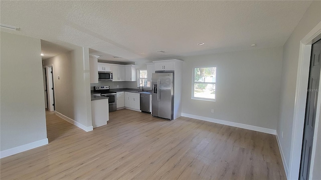 kitchen with sink, a textured ceiling, light wood-type flooring, appliances with stainless steel finishes, and white cabinets