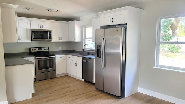 kitchen featuring sink, a textured ceiling, stainless steel appliances, light hardwood / wood-style floors, and white cabinets