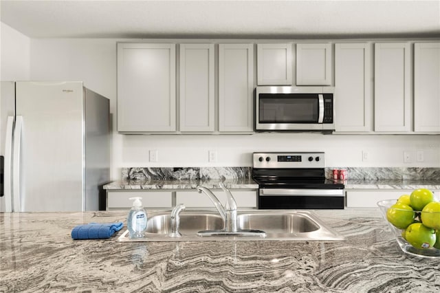 kitchen with gray cabinetry, sink, light stone countertops, and stainless steel appliances