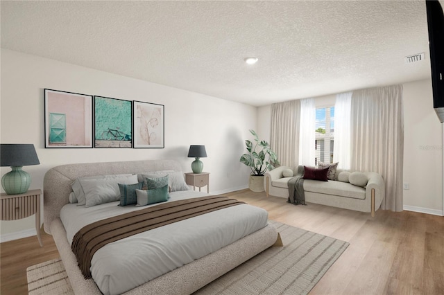 bedroom featuring a textured ceiling, light wood finished floors, visible vents, and baseboards