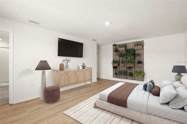 bedroom with a textured ceiling, light wood finished floors, visible vents, and baseboards