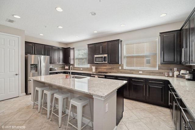 kitchen featuring appliances with stainless steel finishes, a center island with sink, light stone counters, and sink