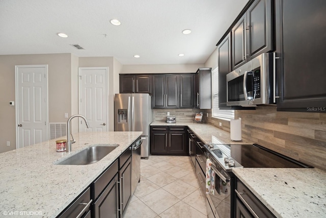 kitchen featuring decorative backsplash, light stone counters, stainless steel appliances, sink, and light tile patterned flooring