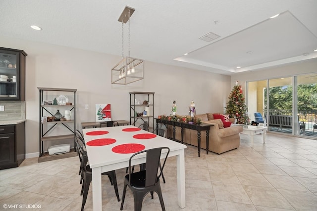 tiled dining room with a raised ceiling and an inviting chandelier