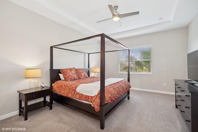 bedroom with a raised ceiling, ceiling fan, and light colored carpet