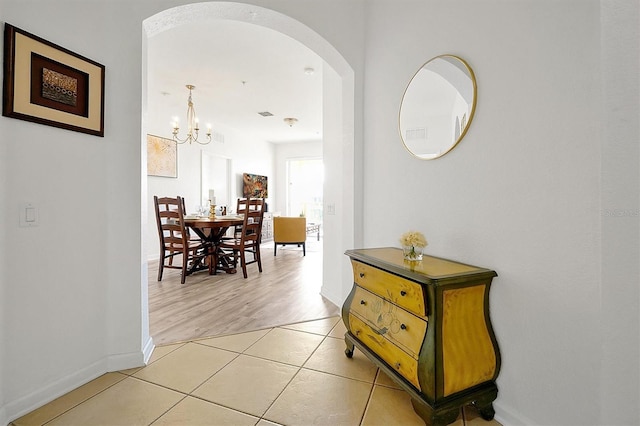 corridor featuring light tile patterned floors and a notable chandelier