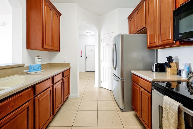 4814 Cayview Ave Unit 40613, Orlando, FL 32819 - kitchen featuring appliances with stainless steel finishes, light countertops, arched walkways, light tile patterned floors, and brown cabinetry