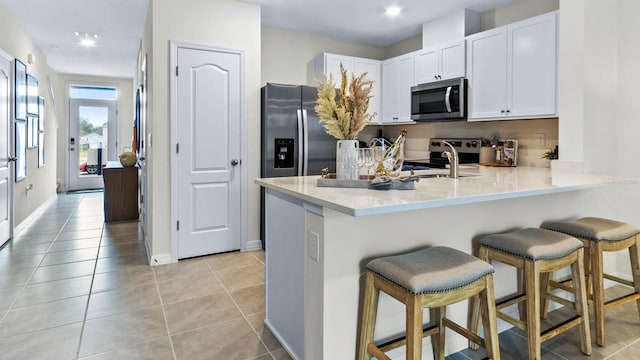 kitchen with kitchen peninsula, a breakfast bar, stainless steel appliances, white cabinets, and light tile patterned flooring